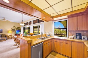 A modern kitchen with wooden cabinets, a stainless steel sink, and a large window offering a view of greenery. - Kapalua Ridge | Ocean View 3 BR, Sleeps 12 | Car Incl. w/ 6+ Nights | KRV ML-3663 by KBM (Lahaina)