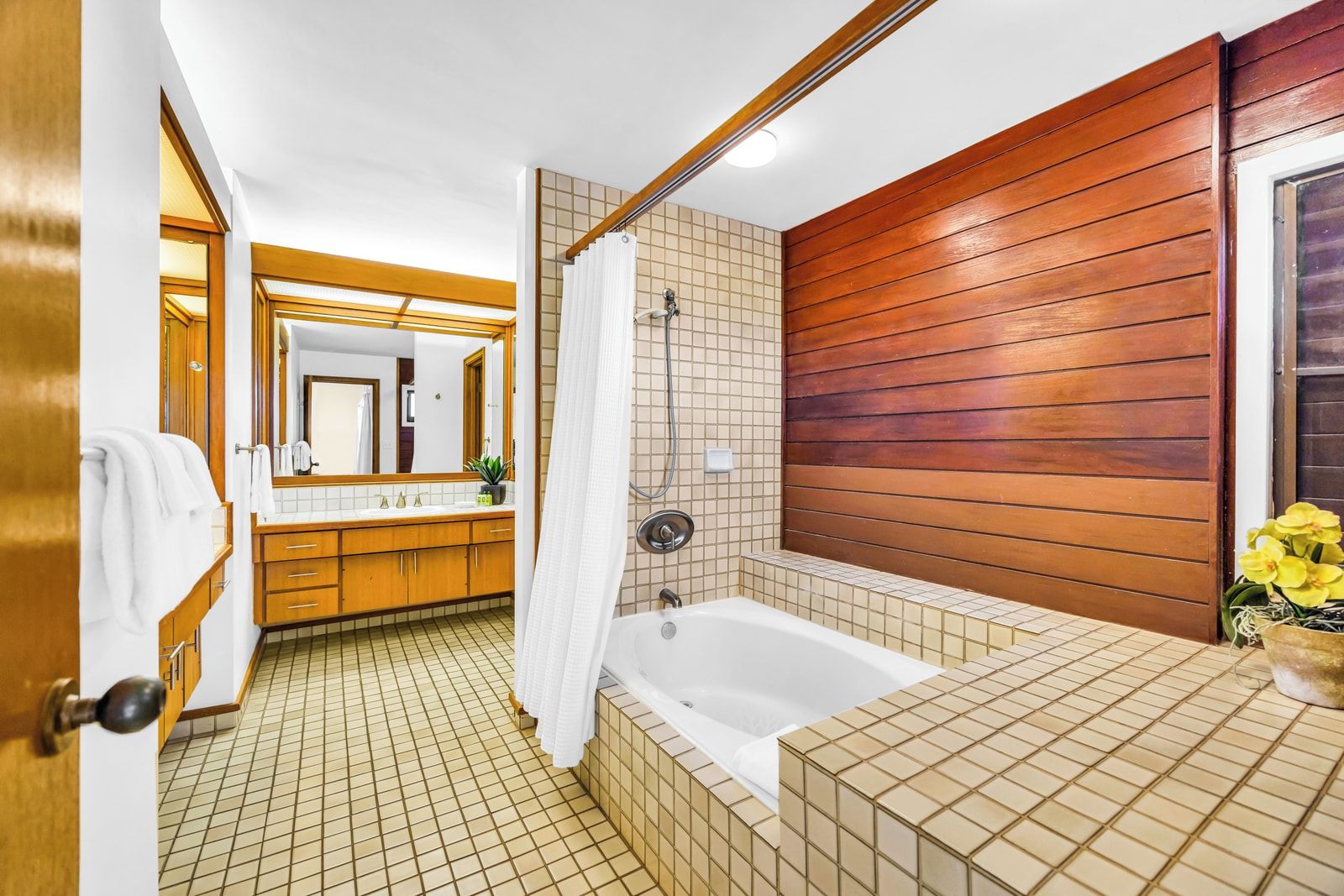 Ein Badezimmer mit einer Badewanne, einer Holzwand, Fliesenboden und einem Spiegel.