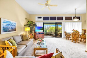 Sala de estar com sofá, mesa de centro, televisão e varanda com mobiliário externo.