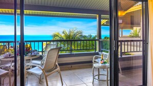 A balcony with a view of the ocean, furnished with white chairs and a table, and a glass door leading to another area. - Kapalua Ridge | Ocean View 3 BR, Sleeps 12 | Car Incl. w/ 6+ Nights | KRV ML-3668 by KBM (Lahaina)