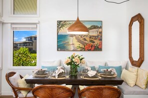 Een eetruimte met een houten tafel gedekt voor vier personen, een schilderij van een strandlandschap erboven en een grote spiegel aan de muur.
