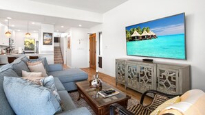 Un salon moderne avec un grand téléviseur à écran plat, un canapé, une table basse et un fauteuil en osier.
