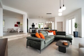 A modern living room with a sectional sofa, a coffee table, and pendant lighting. -  Spacious villa with views of the sea, the Etna volcano, mountains and Taormina. (Sicilia)