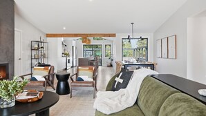 Amplia sala de estar con sofá, mesa de centro y chimenea. Se observa un comedor con mesa y sillas, y una cocina al fondo.