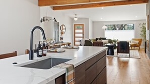 Cocina moderna con una isla grande, vigas de madera y vista a una sala de estar.
