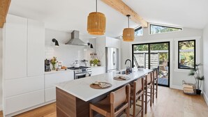 Una cocina moderna con armarios blancos, una isla grande, sillas de madera y luces colgantes.