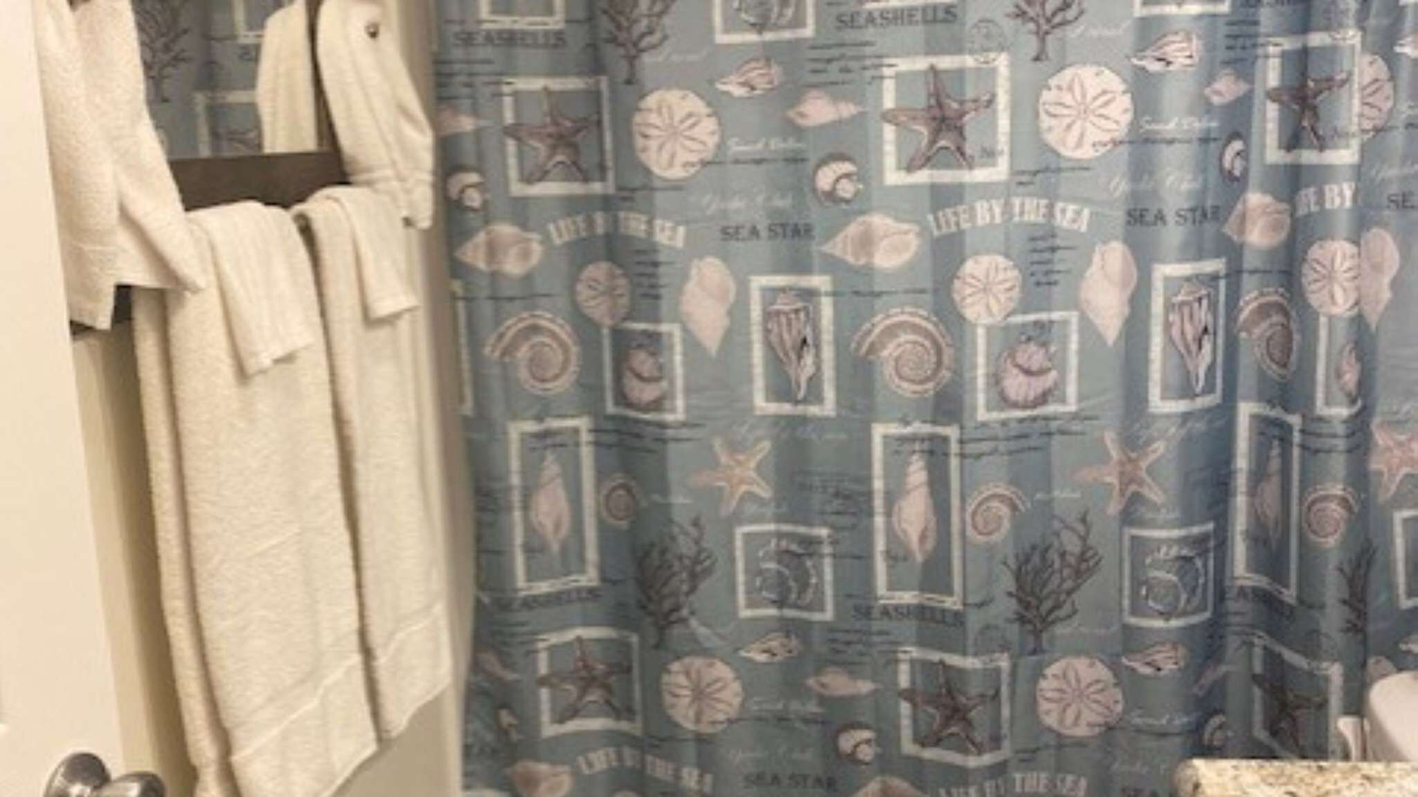 A bathroom with a shower curtain featuring sea-themed designs, a towel rack with towels, and a visible toilet.