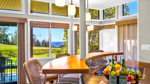 Comedor con vista a un campo de golf y al océano, que incluye una mesa de madera, sillas de mimbre y un frutero con botellas.