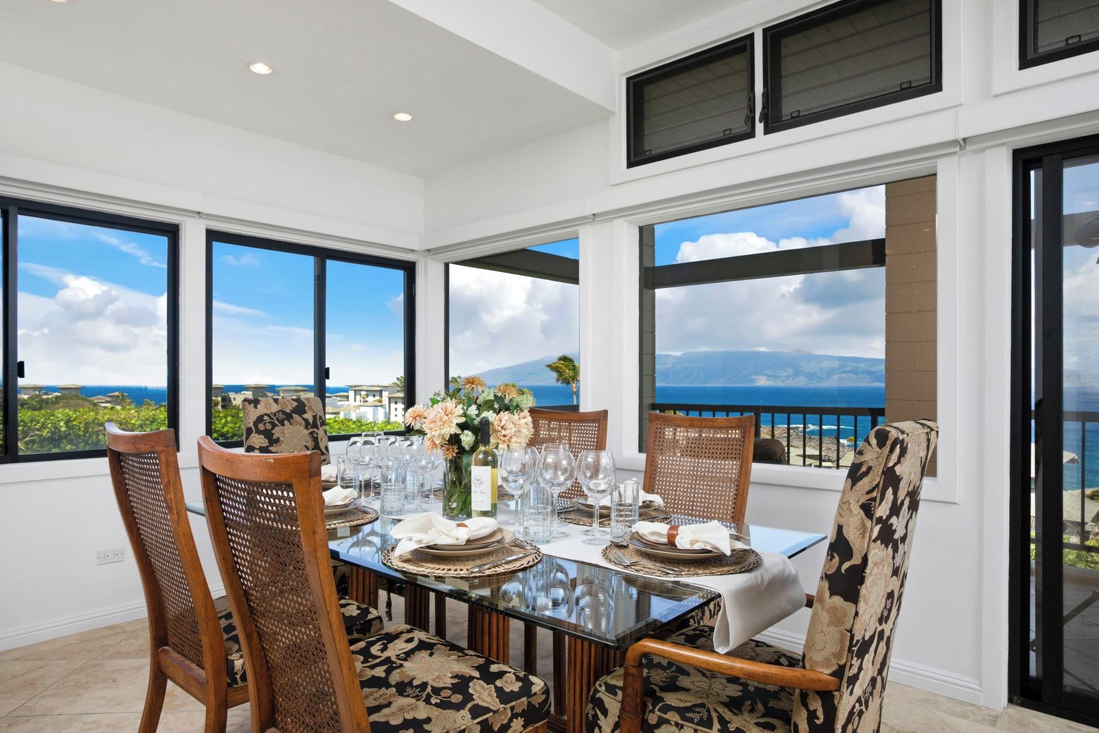 Comedor con una mesa dispuesta para cuatro personas, ventanas amplias con vista al mar y sillas de mimbre.