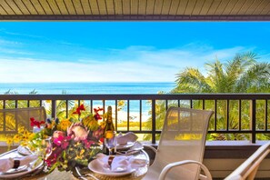 Un balcón con una mesa dispuesta para dos personas, con vista a una playa y al océano.
