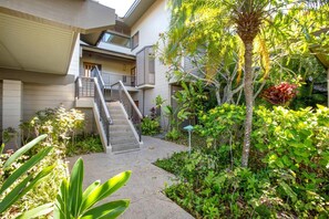 Edificio residencial de varios niveles con una escalera central, rodeado de abundante vegetación y diversas plantas.