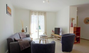 A living room with a sofa, two armchairs, a TV, a bookshelf, and a window with curtains. - Côté Océan - VENSAC - Gîte (VENSAC)