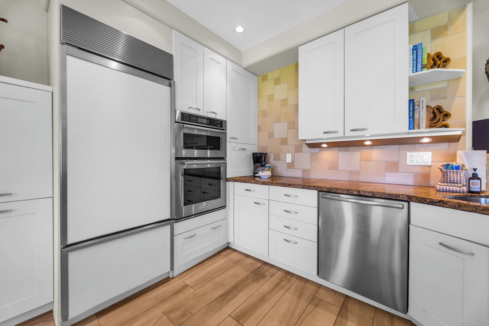 A modern kitchen with white cabinetry, stainless steel appliances, and a wooden floor.