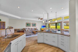A modern kitchen with a central island, white cabinetry, and a dining area with a sofa. - Kapalua Ridge | Ocean View 6 BR, Sleeps 22 | Car Incl. w/ 6+ Nights | KRV ML-3699 by KBM (Lahaina)