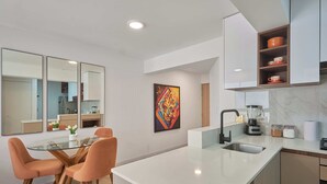 Una cocina moderna con una mesa de comedor de vidrio, sillas naranjas, una encimera blanca y un estante empotrado con vajilla.