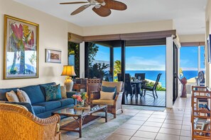Ein Wohnzimmer mit einer Couch, einem Couchtisch und Sesseln, einem Deckenventilator und Meerblick durch große Glasüren.