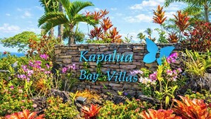 Un cartello di pietra con la scritta 'Kapalua Bay Villas', circondato da piante tropicali e palme.