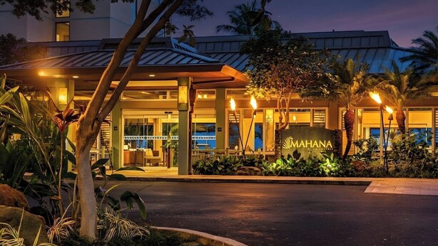 L'ingresso di un hotel con un cartello che riporta 'MAHANA', circondato da piante tropicali e palme.