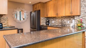 Una cucina con mobili in legno, un piano di lavoro in granito, un frigorifero in acciaio inossidabile e una parete di fondo decorata con un mosaico.
