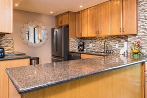 A kitchen with wooden cabinets, a granite countertop, a stainless steel refrigerator, and a backsplash with a mosaic tile pattern. - Mahana Villas | Oceanfront 4 BR Sleeps 11 | Car Incl. w/ 6+ Nights | MAH ML-3714 by KBM (Lahaina)