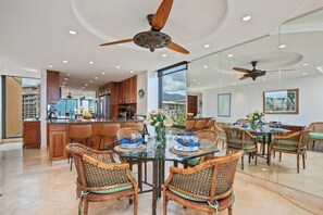 A spacious kitchen with modern appliances, a dining area with wicker chairs, and a large window offering a view of the mountains. - Mahana Villas | Oceanfront 4 BR Sleeps 11 | Car Incl. w/ 6+ Nights | MAH ML-3714 by KBM (Lahaina)