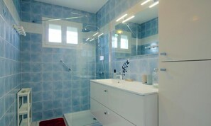 Een badkamer met blauwe tegels, een douche, een wastafel en een spiegel.