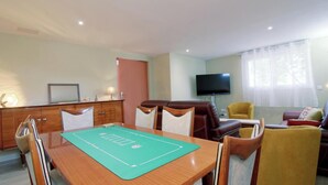 Ein Essbereich mit Tisch, Stühlen, einem Fernseher und einer Couch in einem Raum mit Tür und Fenster.