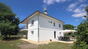 Ein zweigeschossiges weißes Haus mit Balkon, Terrasse und Gartenmöbeln sowie einem Garten.