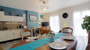 En matplats med ett bord dukat för fyra personer, ett kök i bakgrunden, en klocka på väggen och en takfläkt.