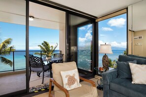 Ein Balkon mit Meerblick, eine Couch, ein Sessel und ein Tisch mit Stühlen.
