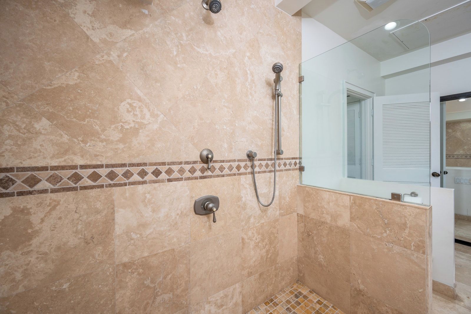 Ducha con cabezal de ducha manual y grifo empotrado, suelo de azulejos y mampara de cristal.