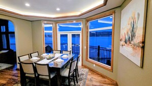 A dining area with a table set for four, large windows with a view of a body of water, and a painting on the wall. - Luxury Waterfront Home, Sleeps 14, 4BR + Bonus Room, Private Beach & Pickleball (Port Orchard)