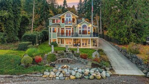 A two-story house with a balcony, surrounded by a well-maintained garden and a stone pathway leading to the entrance. - Luxury Waterfront Home, Sleeps 14, 4BR + Bonus Room, Private Beach & Pickleball (Port Orchard)