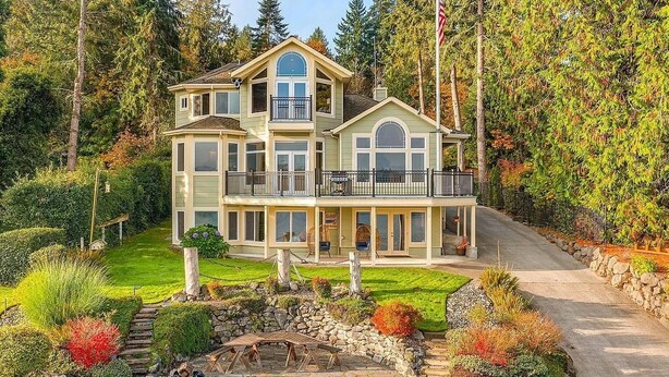 A two-story house with a balcony, surrounded by a garden with a fire pit. - Luxury Waterfront Home, Sleeps 14, 4BR + Bonus Room, Private Beach & Pickleball (Port Orchard)