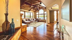 A spacious living room with a wooden ceiling, large windows, a sofa set, and a glass coffee table. - Luxury Waterfront Home, Sleeps 14, 4BR + Bonus Room, Private Beach & Pickleball (Port Orchard)