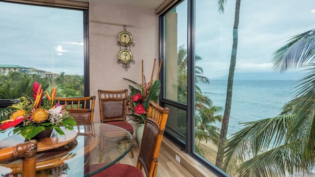 A dining area with a glass table, wicker chairs, and a view of the ocean. - Mahana Villas | Oceanfront 4 BR Sleeps 13 | Car Incl. w/ 6+ Nights | MAH ML-3728 by KBM (Lahaina)