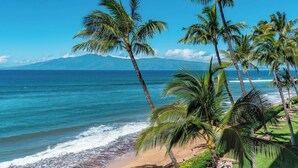 A beach with palm trees, ocean waves, and a mountain in the background. - Mahana Villas | Oceanfront 4 BR Sleeps 13 | Car Incl. w/ 6+ Nights | MAH ML-3728 by KBM (Lahaina)