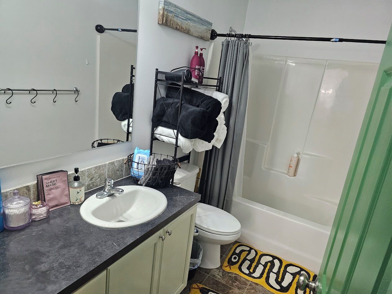 A bathroom with a white sink, a mirror, a towel rack, a shower curtain, and a toilet.