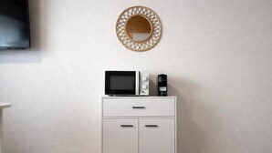 A white cabinet with a microwave and a coffee maker on top, a round mirror on the wall, and a flat-screen TV mounted above the cabinet. - Charming Studio Rheinfall & train station on foot (Neuhausen am Rheinfall)