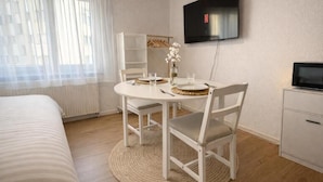 A room with a bed, a dining table with chairs, a TV mounted on the wall, and a small cabinet. - Charming Studio Rheinfall & train station on foot (Neuhausen am Rheinfall)