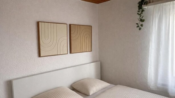 A bedroom with a bed, two pillows, a headboard, and two wall-mounted abstract art pieces. - Charming Studio Rheinfall & train station on foot (Neuhausen am Rheinfall)