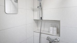 A modern bathroom with a shower, a mirror, and a shelf with toiletries. - Charming Studio Rheinfall & train station on foot (Neuhausen am Rheinfall)