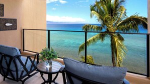 Un balcone con vista sull'oceano, una palma e due sedie con un tavolino e un vaso.
