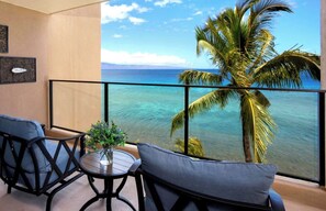 Ein Balkon mit Meerblick, eine Palme und zwei Stühle mit einem kleinen Tisch und einer Vase.