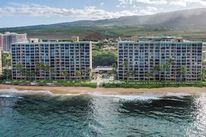A beachfront hotel with multiple high-rise buildings, a beach, and a mountainous backdrop. - Mahana Villas | Oceanfront 4 BR Sleeps 12 | Car Incl. w/ 6+ Nights | MAH ML-3747 by KBM (Lahaina)