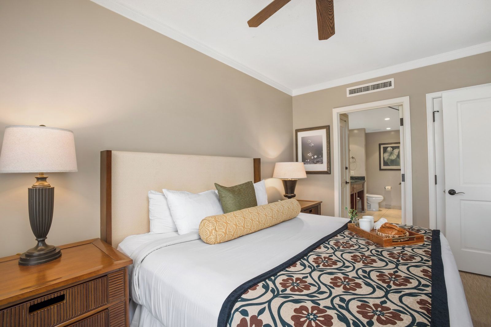 Une chambre d’hôtel avec un lit, des lampes de chevet, une table de nuit et un plateau avec du pain, ainsi qu’une porte donnant sur une salle de bain.