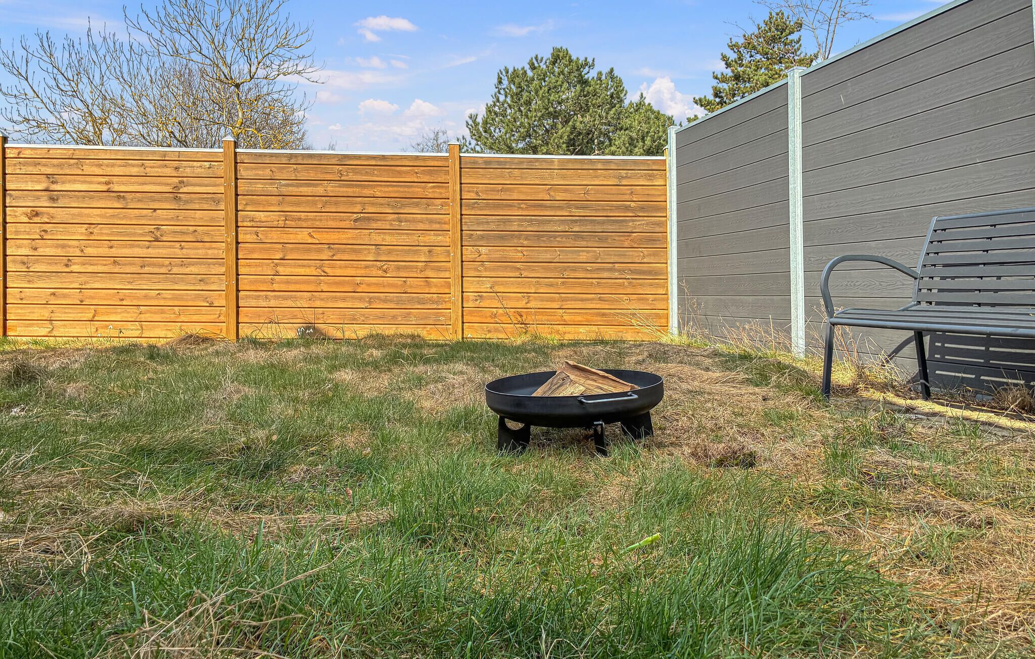 A backyard with a wooden fence, a black grill, and a metal bench.