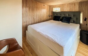 A single bed with a headboard, a wooden floor, and a window with a view.
