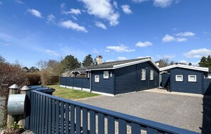 A residential building with a gravel driveway, a wooden fence, and a clear blue sky.
