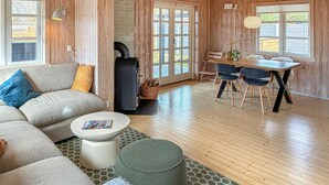 Uma sala de estar aconchegante com sofá, banquinho, mesa de centro e uma mesa de jantar com cadeiras.